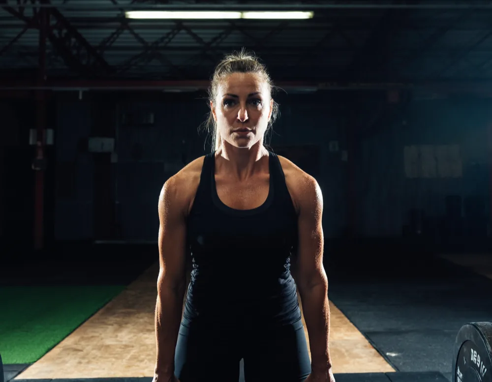 A woman in a black tank top setting up for a deadlift on a wooden lifting platform.