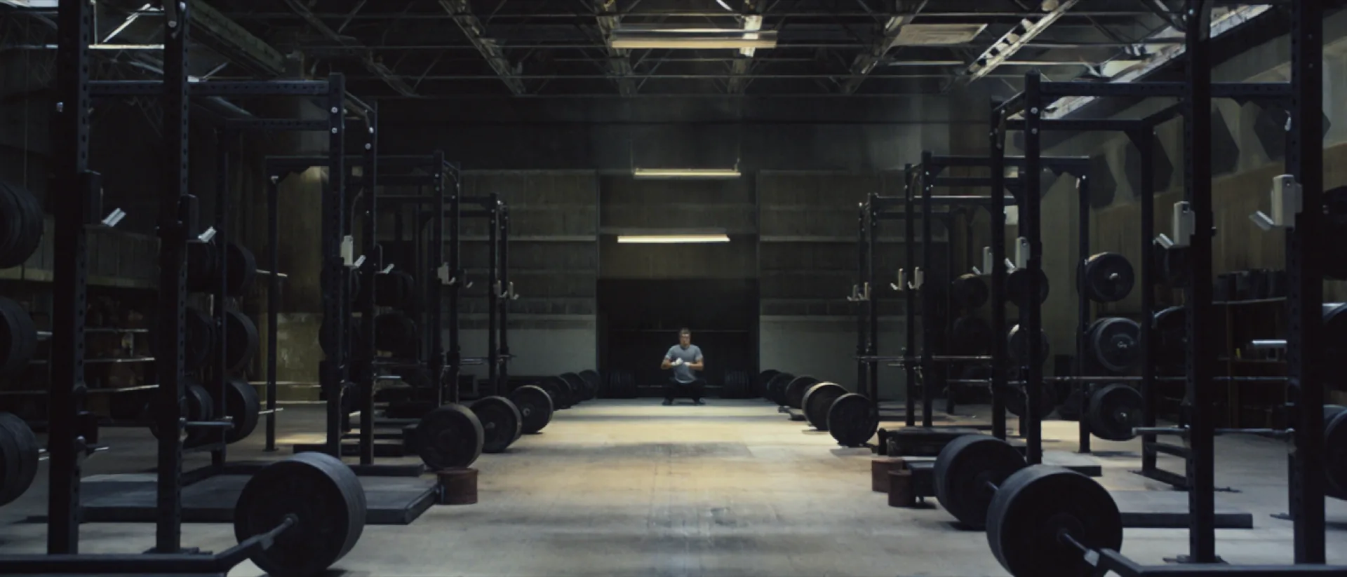 The main hall of Kraftraum Hamborn: two long rows of black power racks and loaded barbells under industrial lighting, a lifter chalking his hands at the far end.
